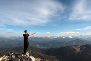 Bergsteiger steht auf Felsbrocken mit ausgebreiteten Armen in Richtung Gebirge Bergsteiger steht auf Felsbrocken mit ausgebreiteten Armen in Richtung Gebirge